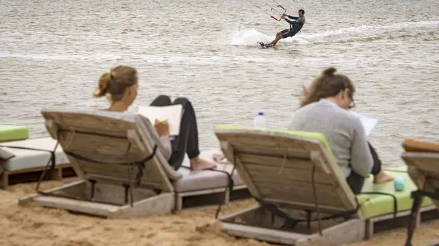 European tourists relaxing on sun loungers in Western Sahara, with another kitesurfing in the ocean